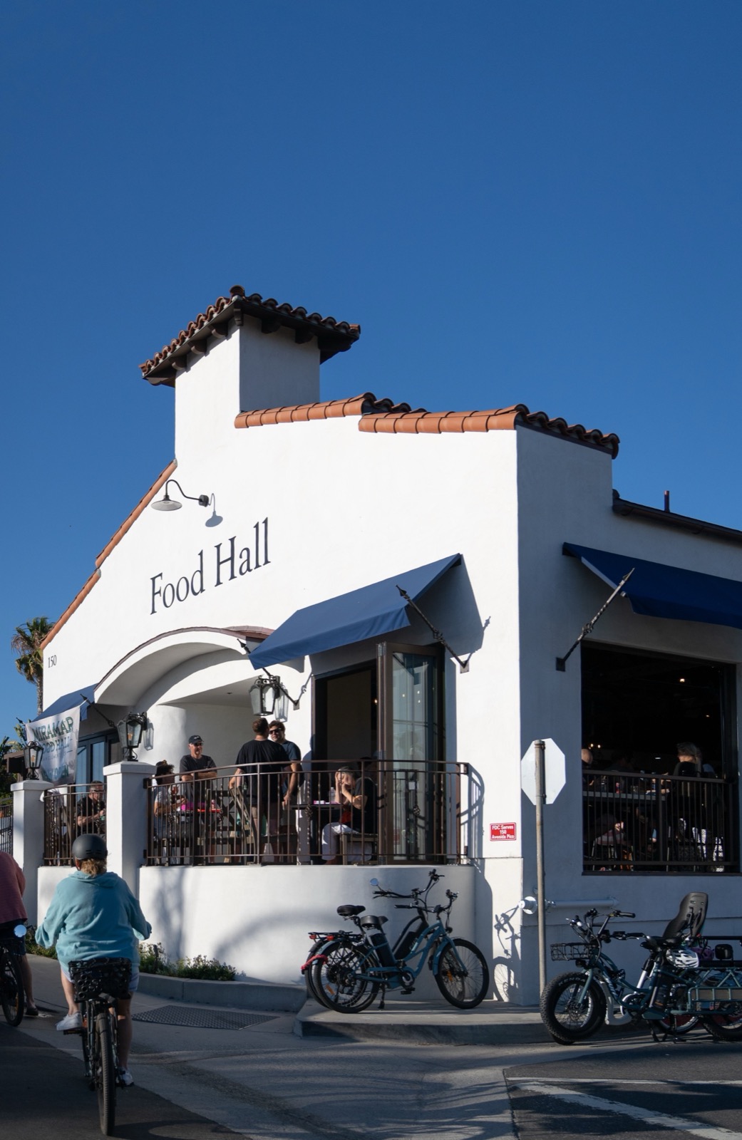 The Spanish-style exterior of Miramar Food Hall at 150 W Avenida Pico, San Clemente, with guests dining on the arched balcony